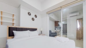 A hotel room with a bed, a nightstand, a lamp, and a sliding glass door leading to a bathroom. - Homey And Simply Look 1Br Tamansari Bintaro Mansion Apartment (South Tangerang)