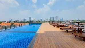 A rooftop pool with wooden deck and lounge chairs, overlooking a cityscape. - Homey And Simply Look 1Br Tamansari Bintaro Mansion Apartment (South Tangerang)