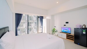 Una habitación de hotel moderna con una cama grande, un televisor, un refrigerador y una ventana con cortinas.