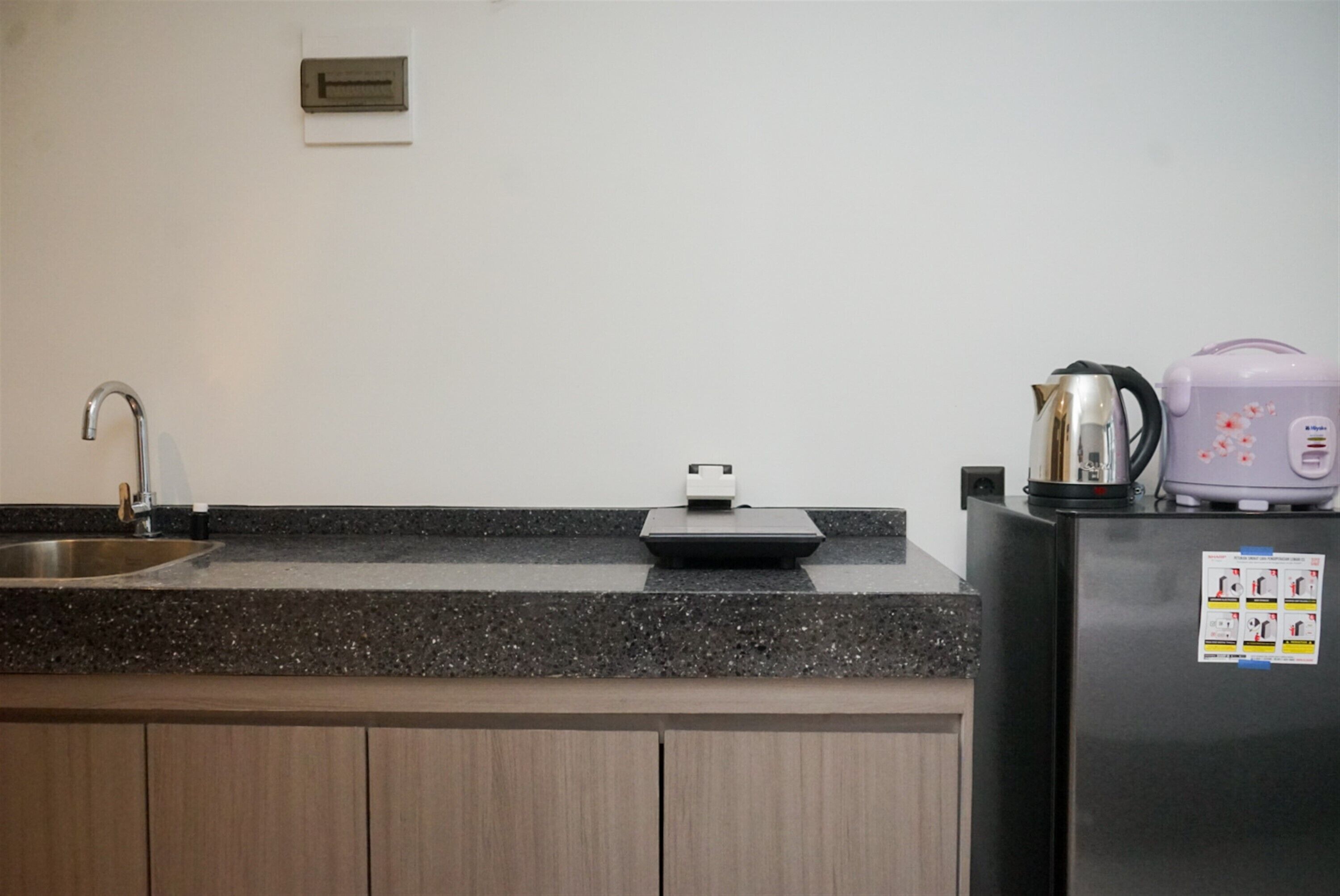 A kitchen with a granite countertop, stainless steel sink, and a black refrigerator with a kettle on top.
