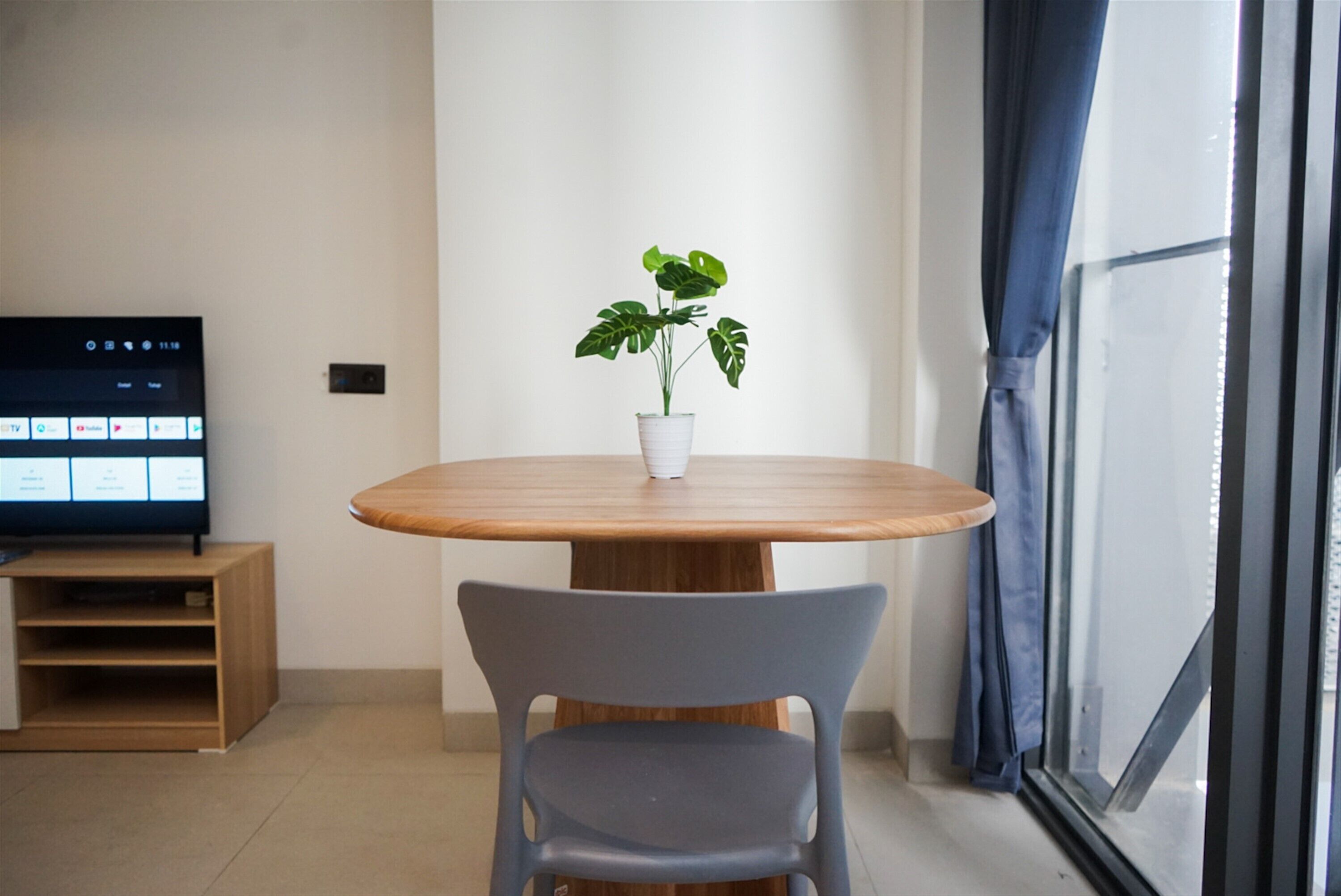A modern room with a wooden dining table, a potted plant, a flat-screen TV, and a window with curtains.