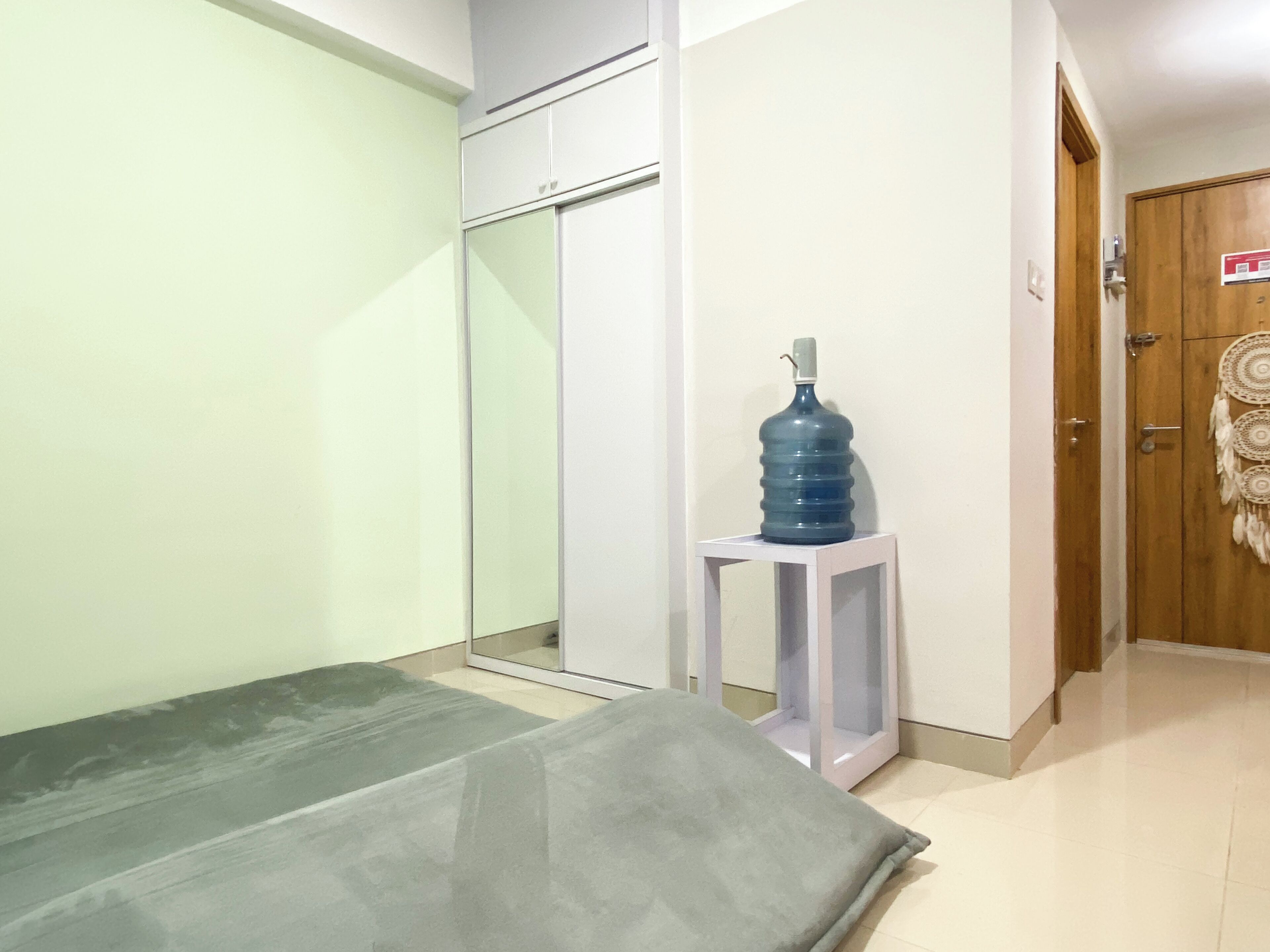 A hotel room with a bed, a water dispenser, a wardrobe, and a door with a decorative item.