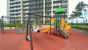 A playground with swings and slides, surrounded by a red surface, in front of a multi-story building. - Well Furnished Studio Room Daan Mogot City Apartment (Jakarta)