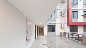 Un corredor moderno de hotel con barandilla de vidrio, una escalera y vista al exterior del edificio.