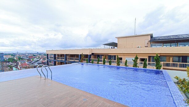 Una piscina en la azotea con un deck de madera, rodeada por un edificio con varios balcones y vistas a la ciudad.