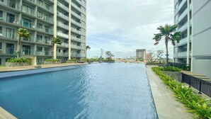 Una piscina rodeada de edificios modernos, con palmeras y un cielo despejado.