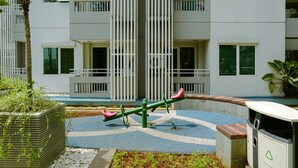 A playground with seesaws and a recycling bin, surrounded by a building with balconies and windows. - Comfy And Homey 1Br At Sky Terrace Apartment (Jakarta)
