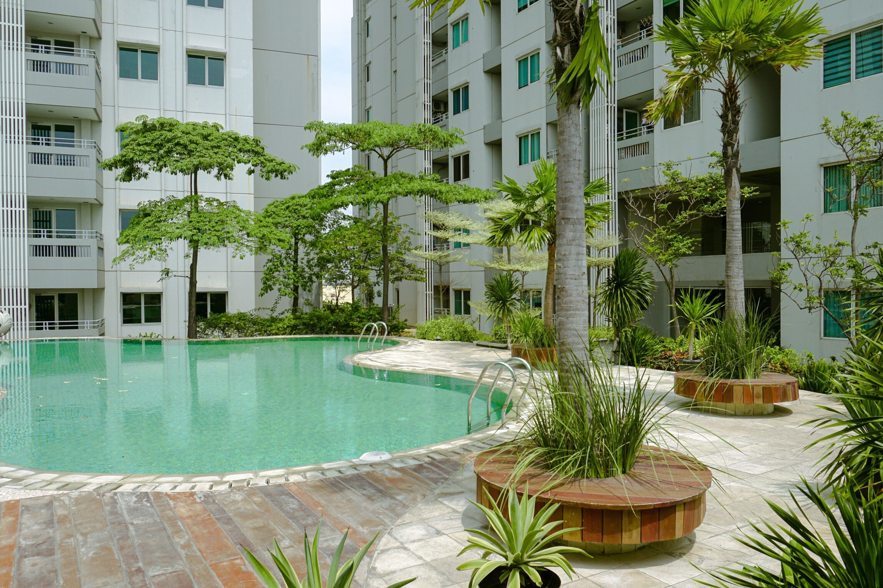 A swimming pool surrounded by potted plants and a multi-story building with balconies.