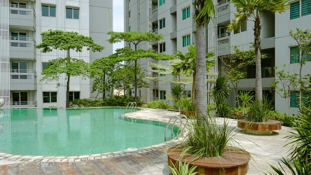 A swimming pool surrounded by potted plants and a multi-story building with balconies. - Comfy And Homey 1Br At Sky Terrace Apartment (Jakarta)