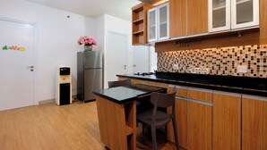 A compact kitchen with wooden cabinets, a black countertop, and a tiled backsplash. - Combined And Spacious 3Br At Green Pramuka City Apartment (Jakarta)