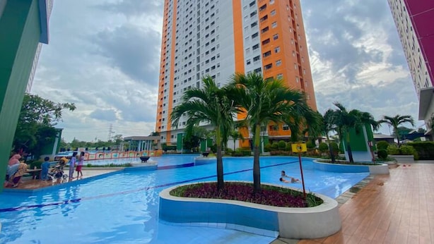 A swimming pool area with a tall building in the background, surrounded by palm trees and a paved walkway. - Combined And Spacious 3Br At Green Pramuka City Apartment (Jakarta)