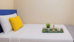A bed with white bedding, a blue headboard, and two pillows, one white and one yellow. - Combined And Spacious 3Br At Green Pramuka City Apartment (Jakarta)