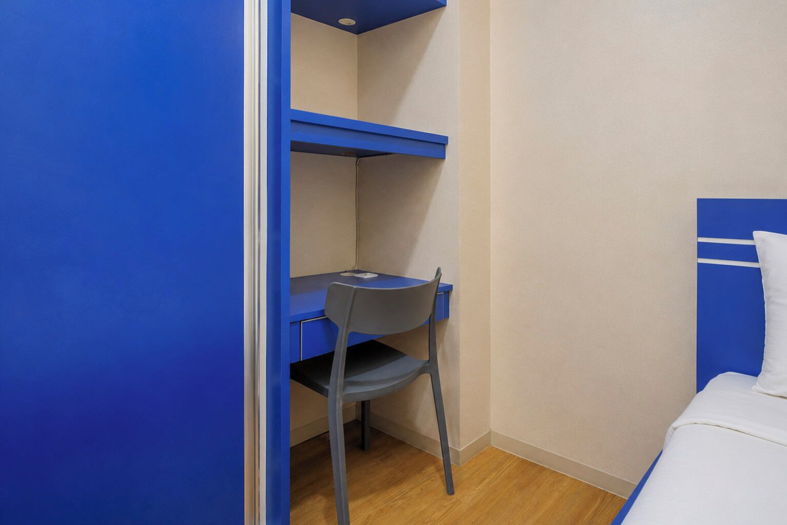 A small room with a single bed, a desk with a chair, and a blue wall.