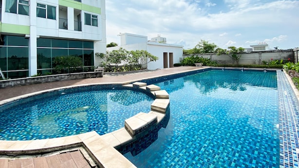 A modern building with a rooftop swimming pool, surrounded by greenery and a clear sky. - Enjoy Living Studio At Enviro Apartment (Cikarang)