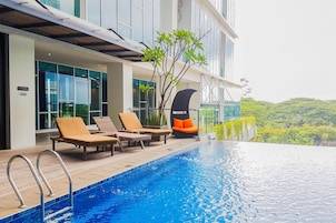 Un hotel moderno con piscina infinita en la azotea, sillones de descanso y vistas a la vegetación circundante.