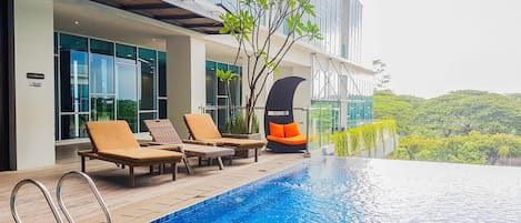 Un hôtel moderne doté d’une piscine à débordement sur le toit, de chaises longues et offrant une vue sur la verdure environnante.