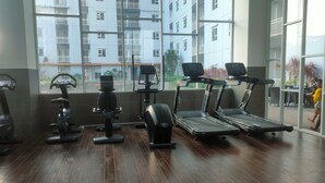 Ein Fitnessstudio mit Trainingsgeräten, großen Fenstern und Blick auf ein Wohngebäude.