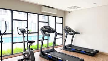 A gym with treadmills, an elliptical, and a pool visible through large windows.