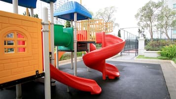 A playground with a red slide, a green climbing area, and a yellow playhouse.