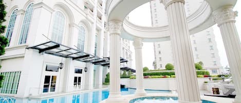 Un espace piscine intérieur luxueux, doté d’une architecture classique, comprenant des colonnes et une pergola.