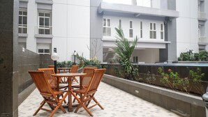 A terrace with a table and chairs, a planter with plants, and a view of a building with windows and balconies. - Best Choice And Cozy Living 2Br At Bale Hinggil Apartment (Surabaya)