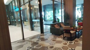 Un hall d’entrée moderne avec une cloison en verre, un espace détente avec un canapé et des fauteuils, et un sol à motifs.