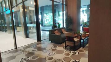 A modern lobby with a glass partition, a seating area with a sofa and armchairs, and a patterned floor.
