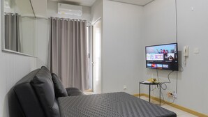 Ett rum med en säng, en tv som är monterad på väggen, ett litet bord och en gardin.
