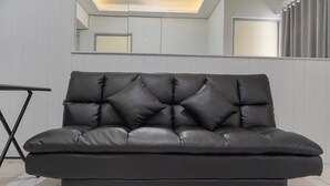 En svart lädersoffa med ett knappstoppat ryggstöd och fyra armstöd, placerad i ett modernt rum med vita väggar och ett kaklat golv.