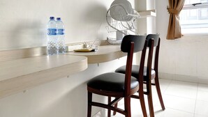Una habitación con escritorio de madera, dos sillas, dispensador de agua, tetera y ventana con cortinas.