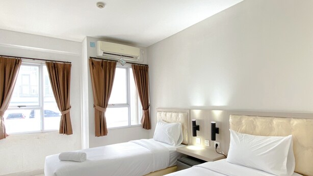 Una habitación de hotel con dos camas, una ventana con cortinas, un aire acondicionado y una mesita de noche con lámpara.