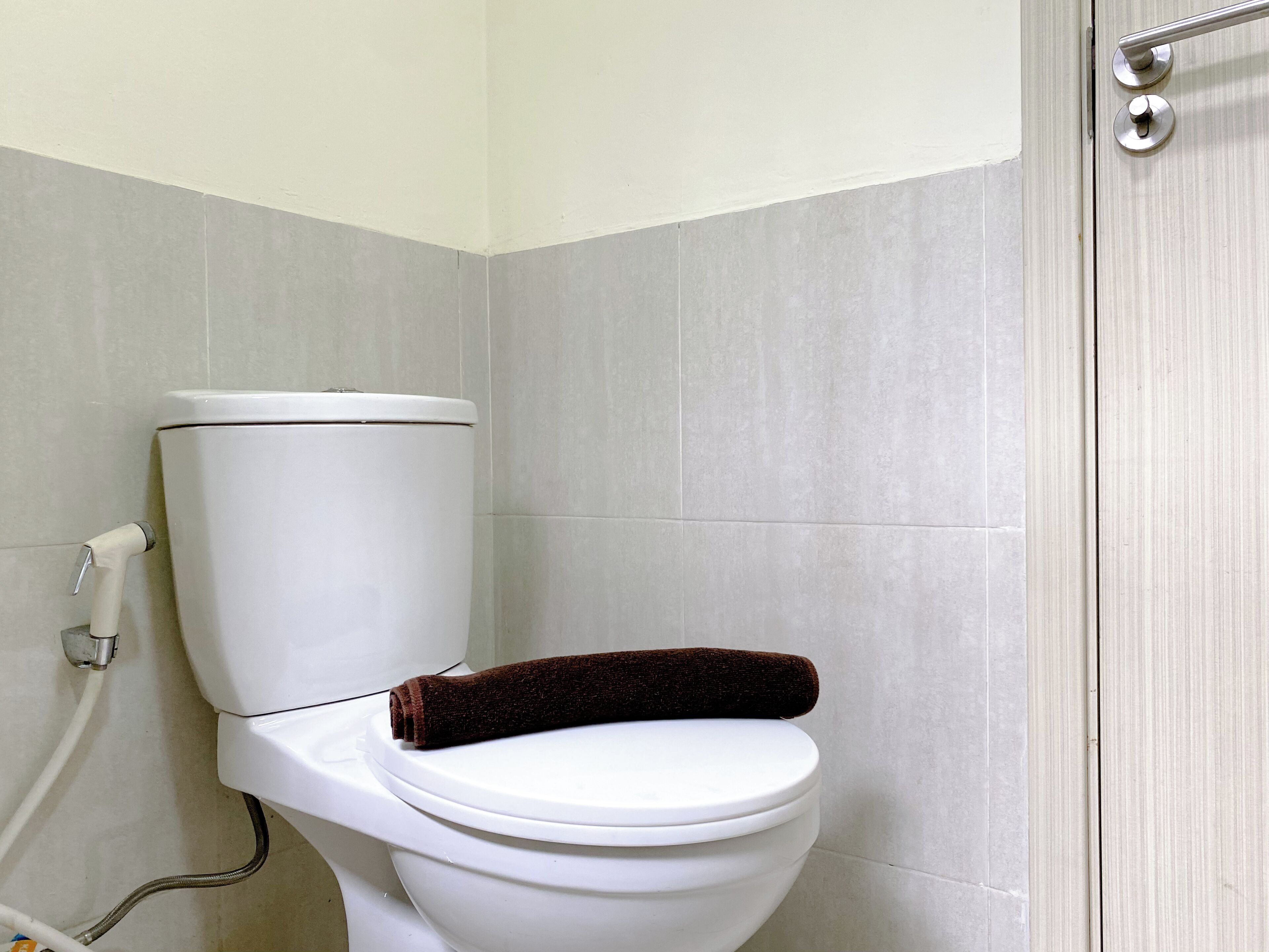 A white toilet with a brown towel on the seat, a metal handrail, and a white pipe on the left.