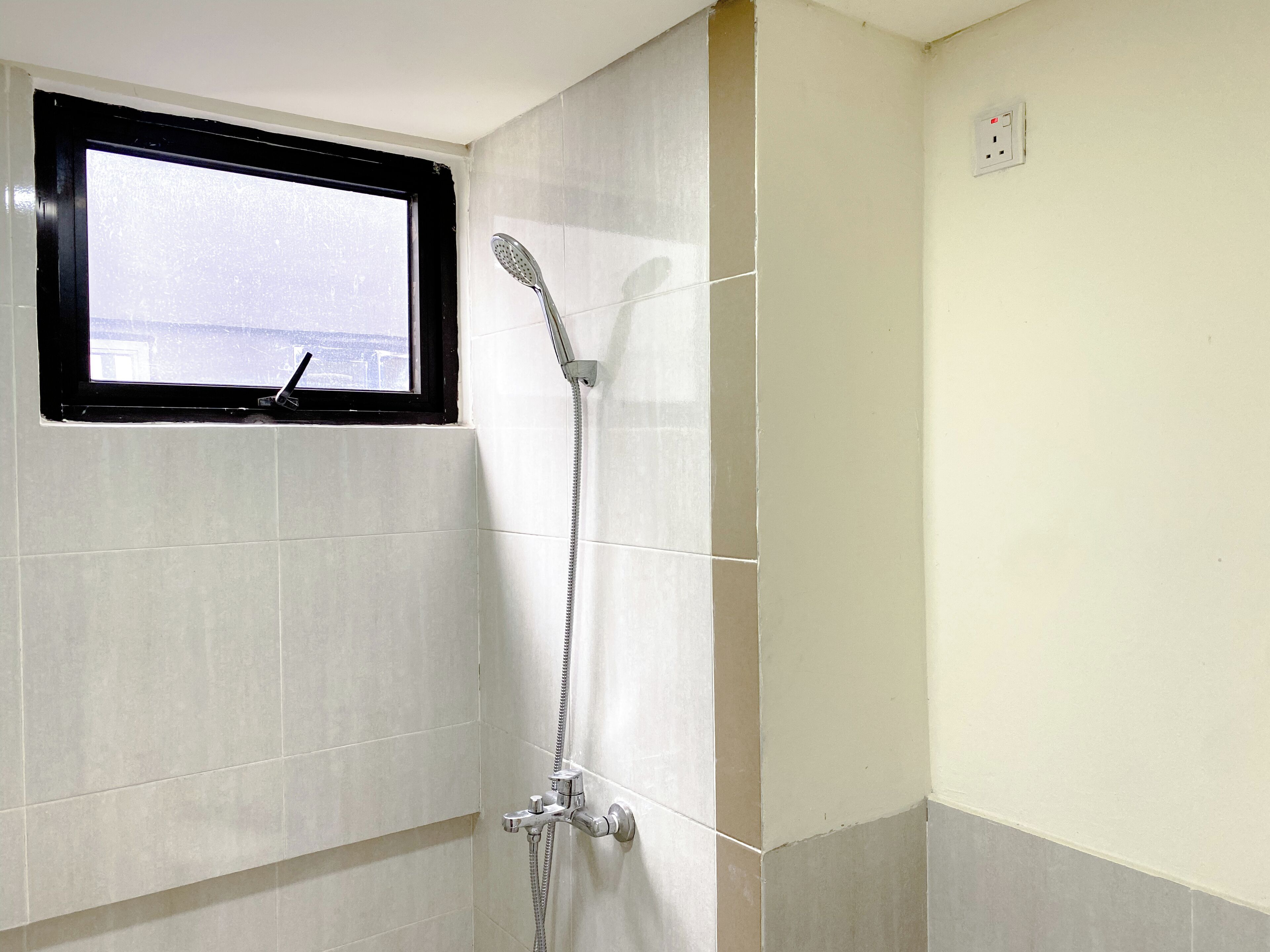 Een badkamer met een douche, een raam en een lichtschakelaar aan de muur.