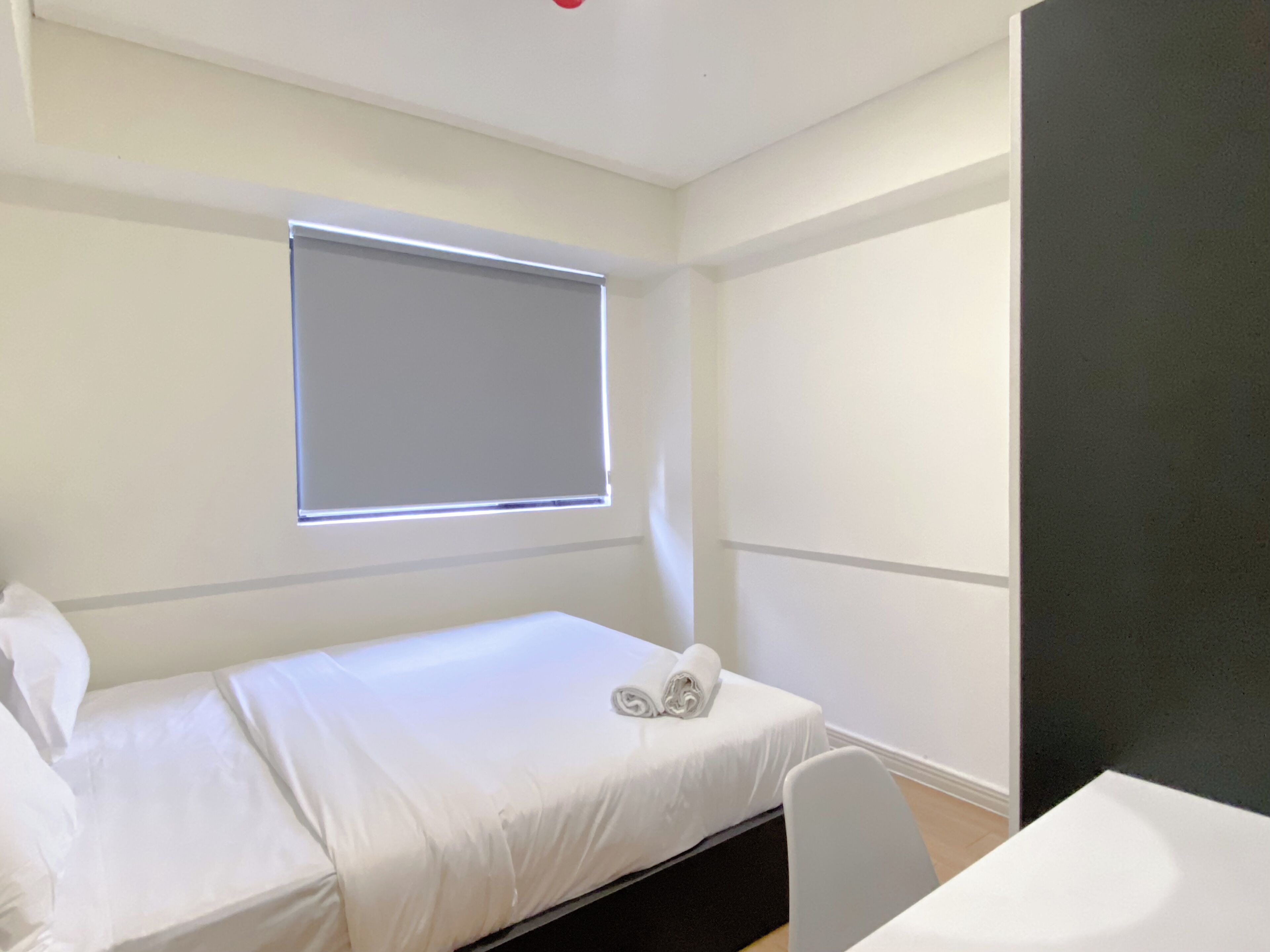 Un dormitorio pequeño y ordenado con una cama individual, una ventana con persianas, una mesita de noche y una silla.