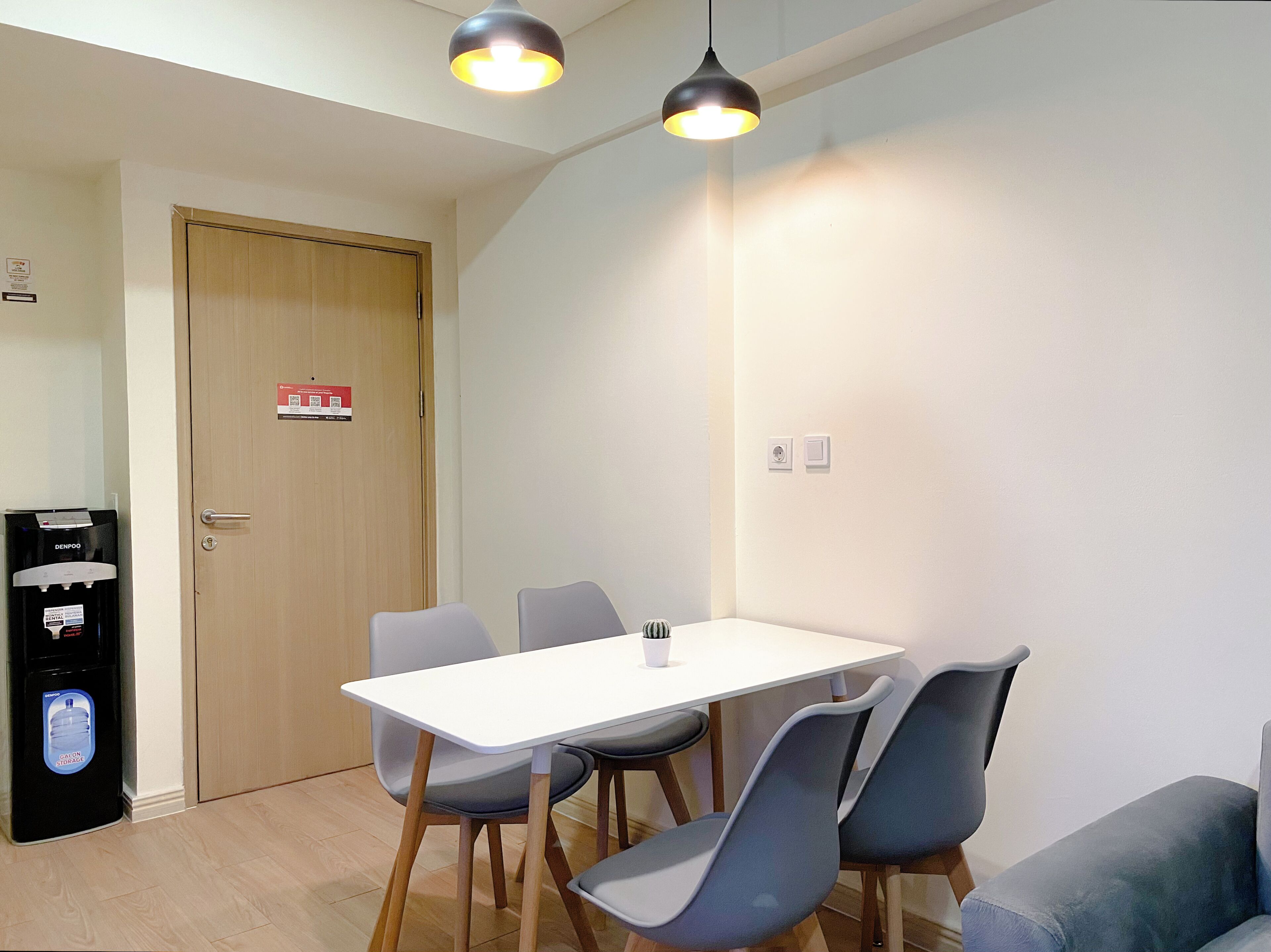 A dining area with a white table and four chairs, a water dispenser, and a door with a fire safety sign.