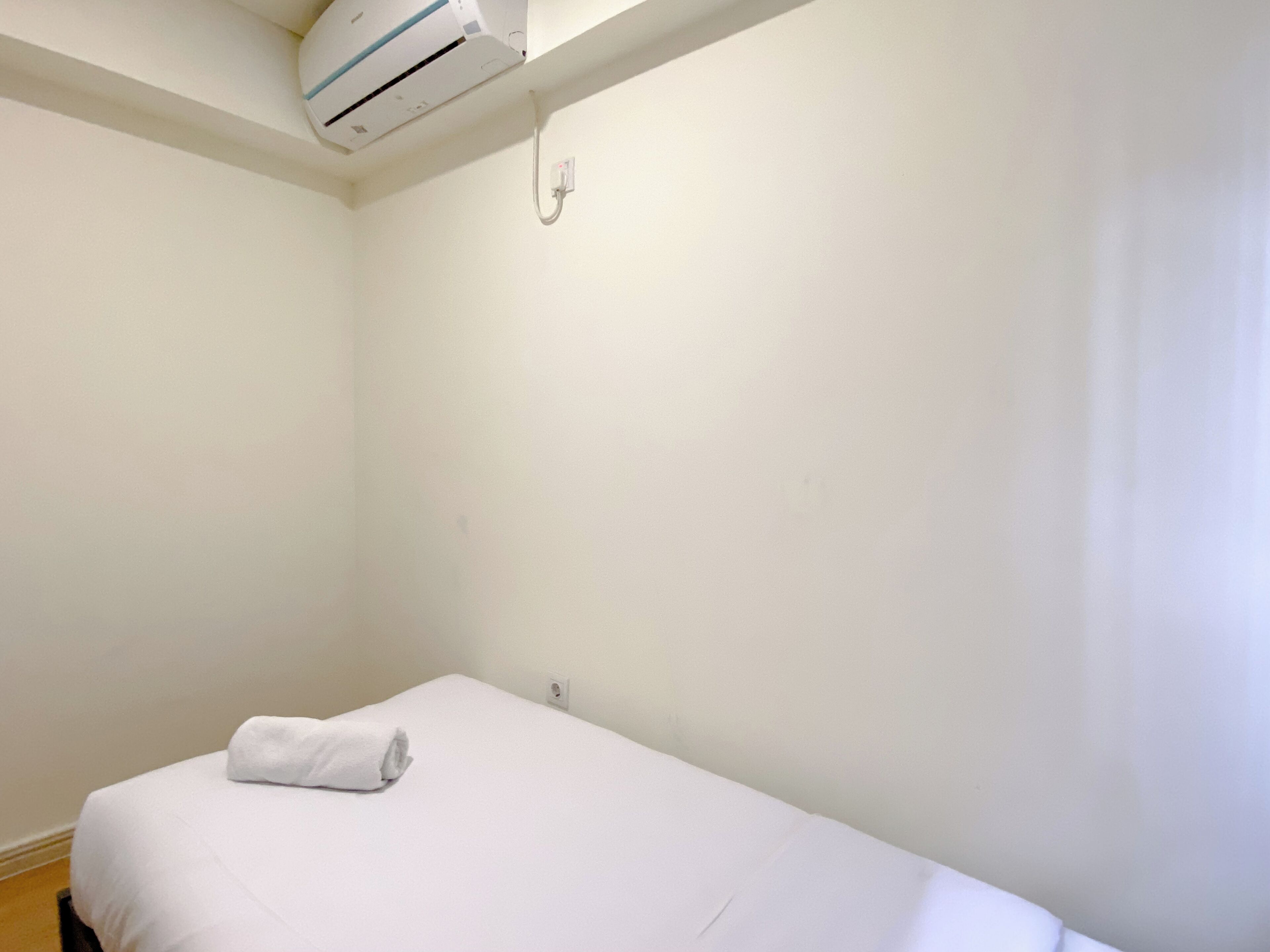 A small, white, single-bed room with a white air conditioning unit mounted on the ceiling.