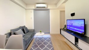 A modern living room with a grey sofa, a coffee table, a flat-screen TV on a stand, and a patterned rug. - Comfort 2Br With Work Space At Meikarta Apartment (Cikarang)