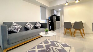 A modern living room with a grey sofa, patterned cushions, a small round table with a plant, and a patterned rug.