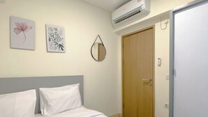 A hotel room with a bed, a wooden door, and wall-mounted air conditioning unit.