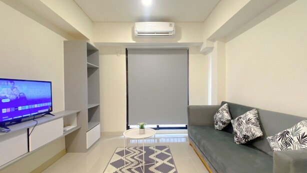 A modern living room with a grey sofa, patterned rug, and a flat-screen TV on a white stand.