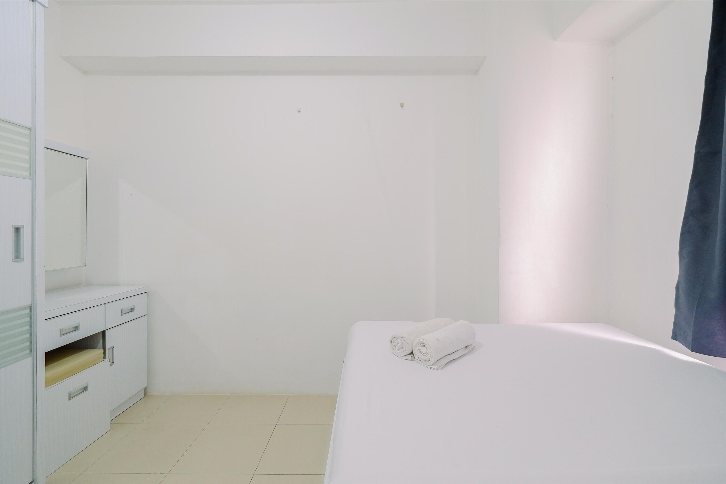 A minimalist hotel room with a bed, a small bedside table, and a wardrobe.