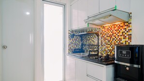 A kitchen with white cabinets, a colorful tiled backsplash, a black coffee machine, and a window.