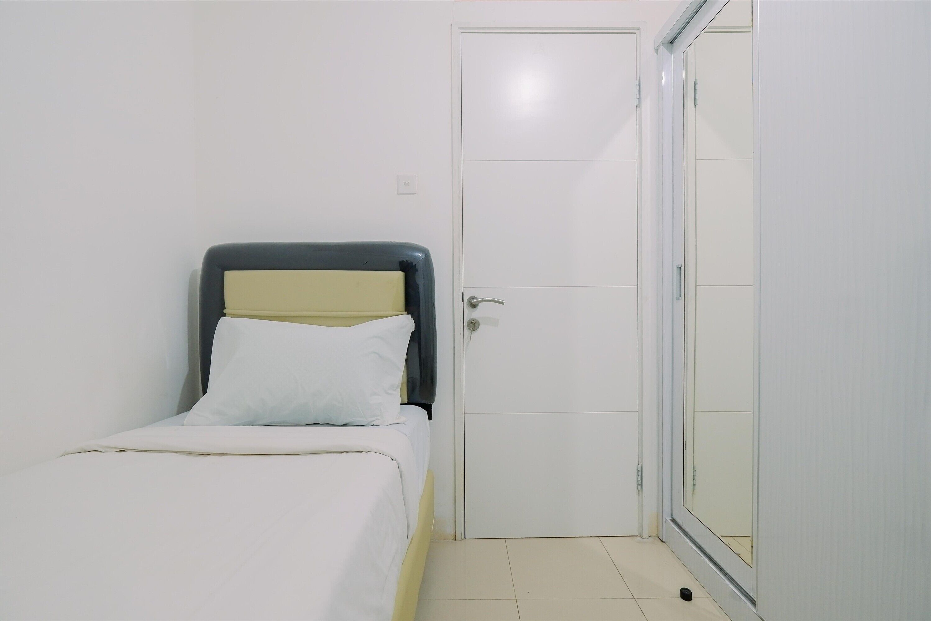 Una stanza piccola e pulita con un letto singolo, una porta e un pavimento piastrellato.