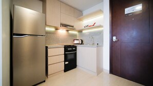 A compact kitchen with a refrigerator, oven, microwave, and a coffee maker on the countertop. - Modern And Comfy Studio At Grand Sungkono Lagoon Apartment (Surabaya)