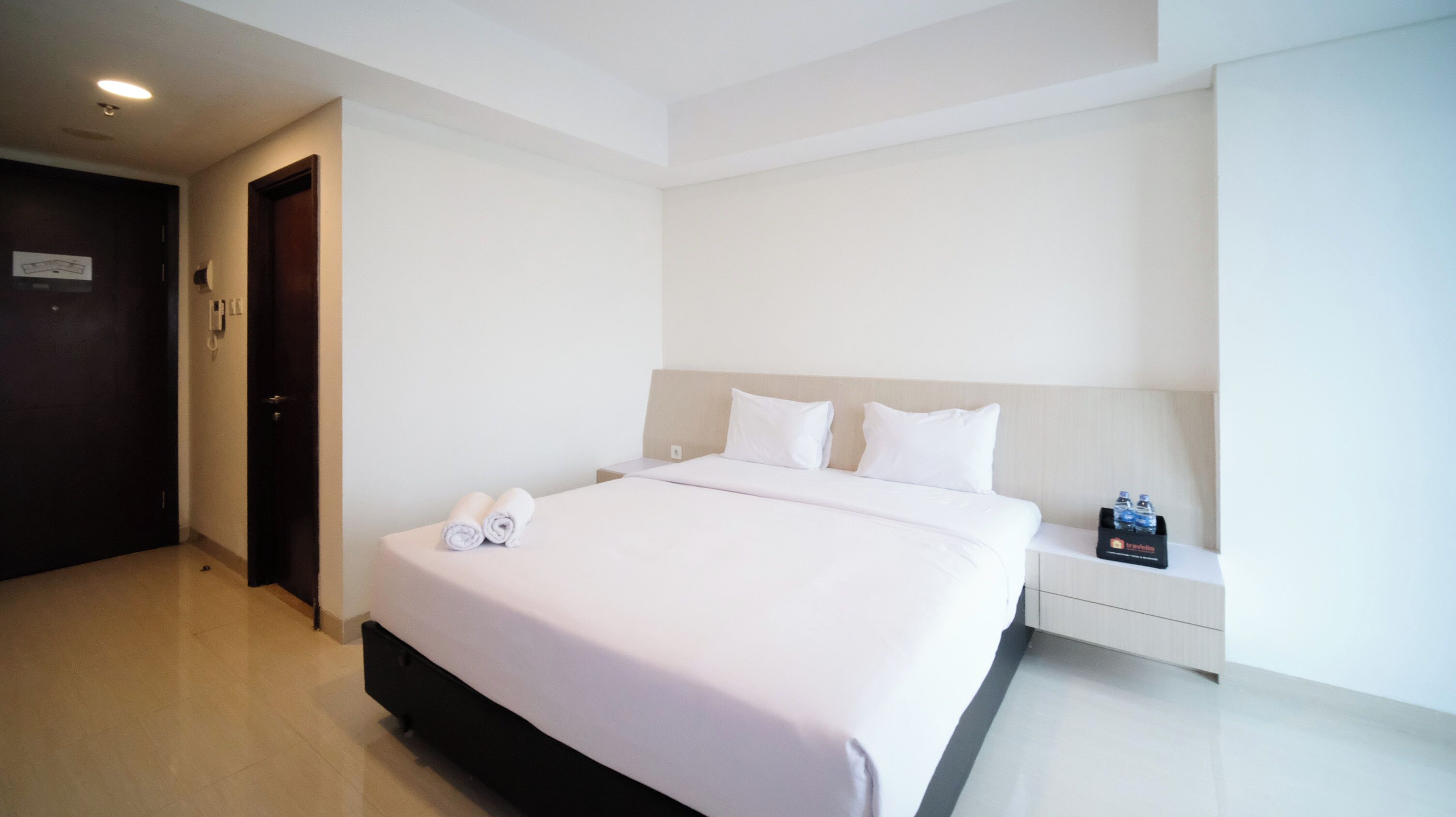 A hotel room with a large bed, a bedside table with a water bottle, and a door with a sign.