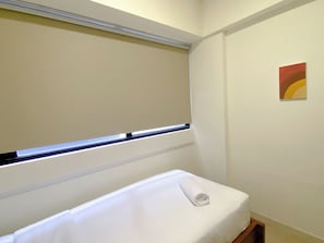 A room with a bed, a window with blinds, and a painting on the wall.