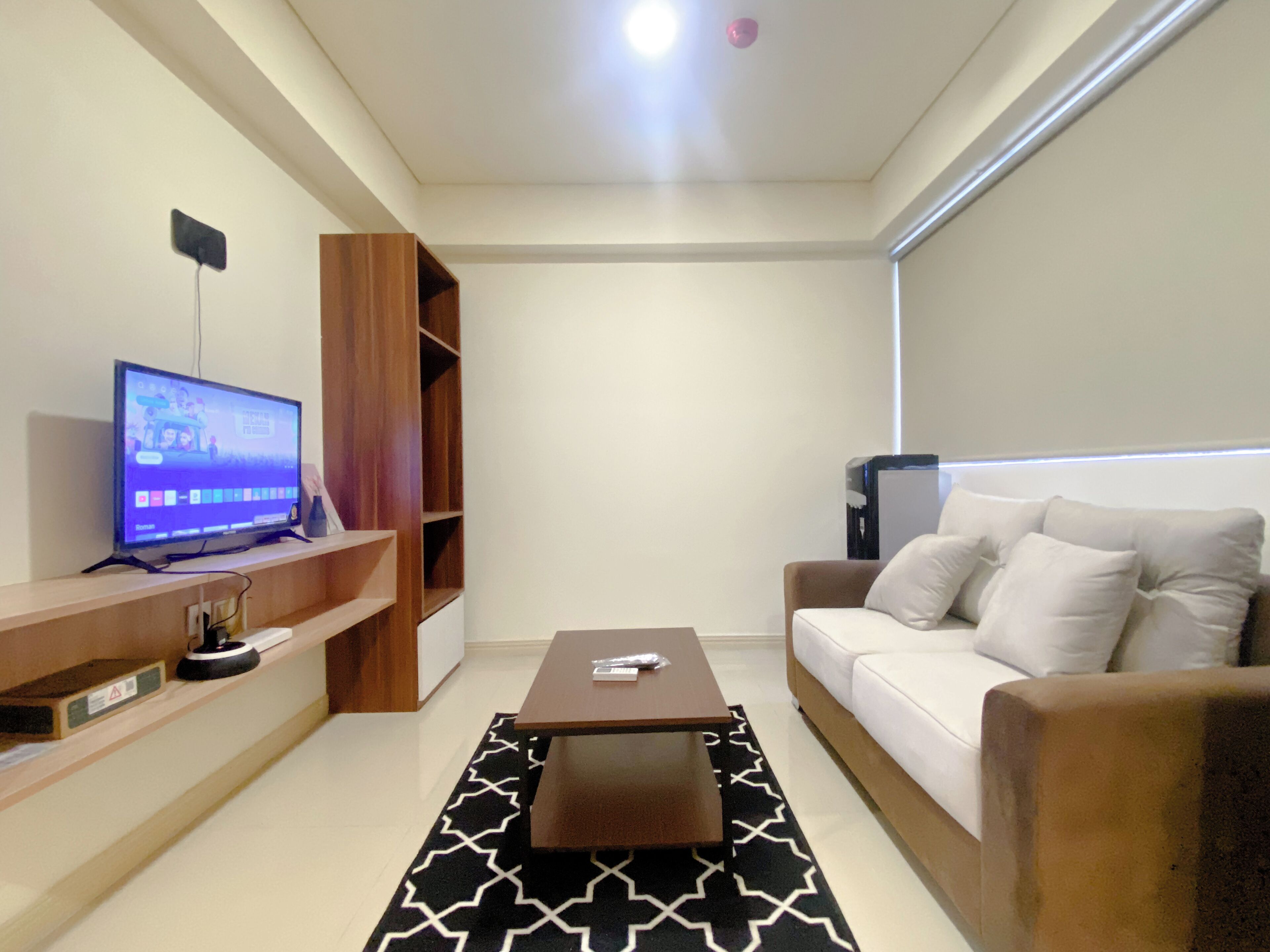 Een moderne woonkamer met een flatscreen televisie, een houten tv-meubel, een bruine salontafel, een witte bank en een kamerkleed met een patroon.