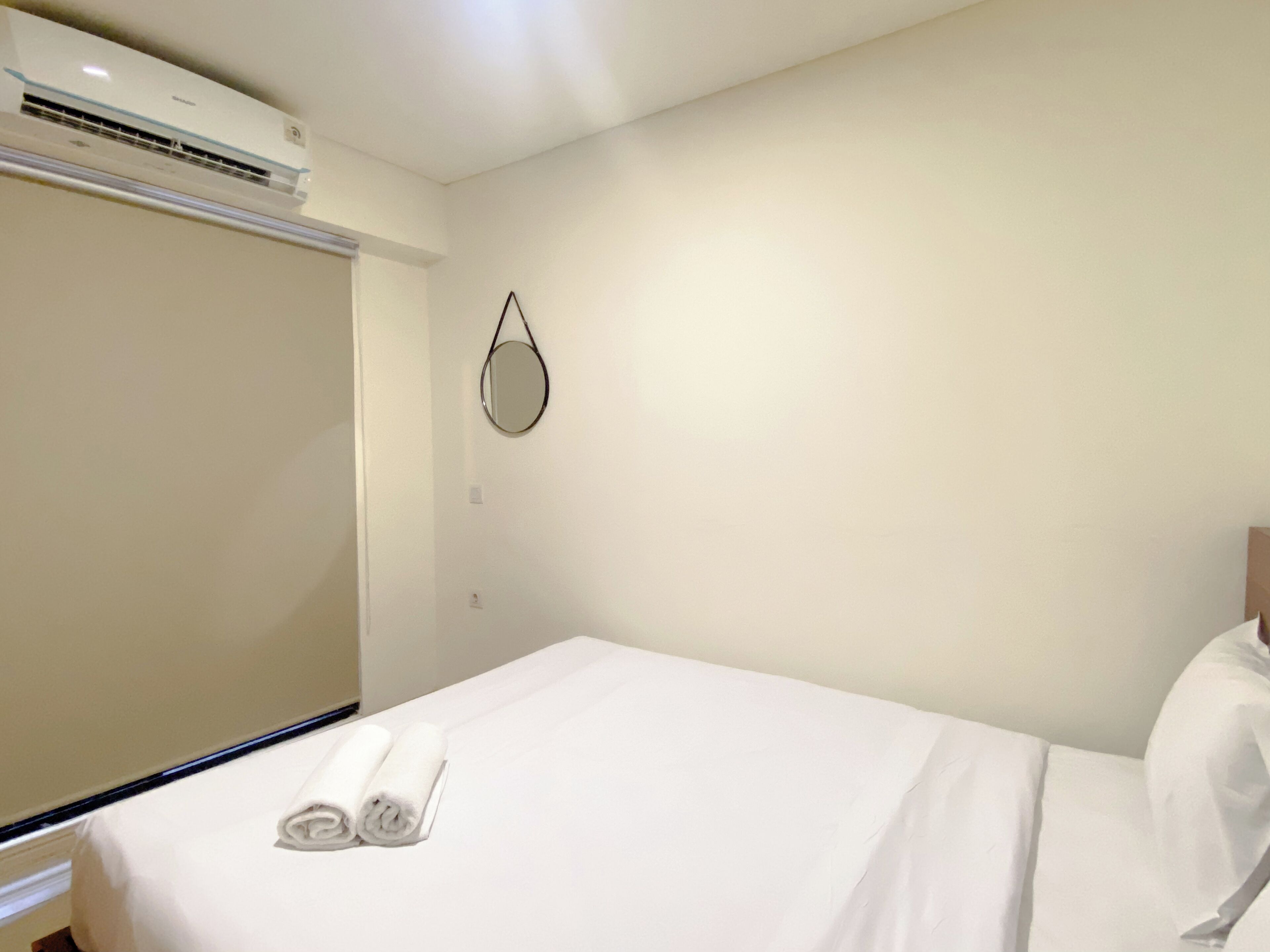 A hotel room with a bed, a wall-mounted mirror, and an air conditioning unit.