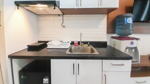 Una cocina compacta con armarios blancos, una encimera negra, un lavamanos de acero inoxidable y un dispensador de agua.