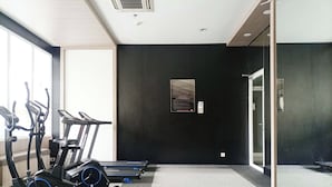 Un gimnasio con bicicletas estáticas, cintas de correr y un espejo grande.